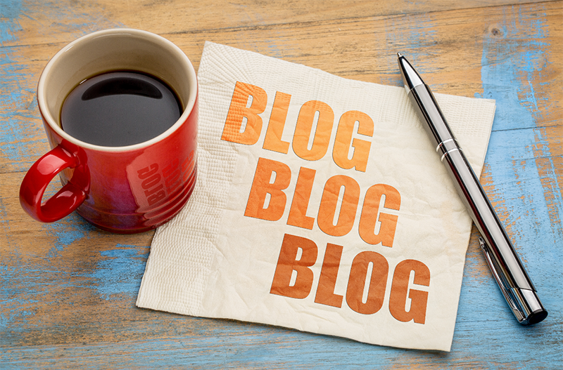 a cup of coffee, napkin, and pen sitting on an painted wood surface. The napkin has the words 'blog blog blog' on it