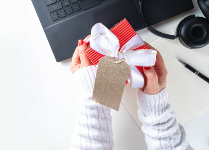 Womens hands holding a christmas gift over a laptop