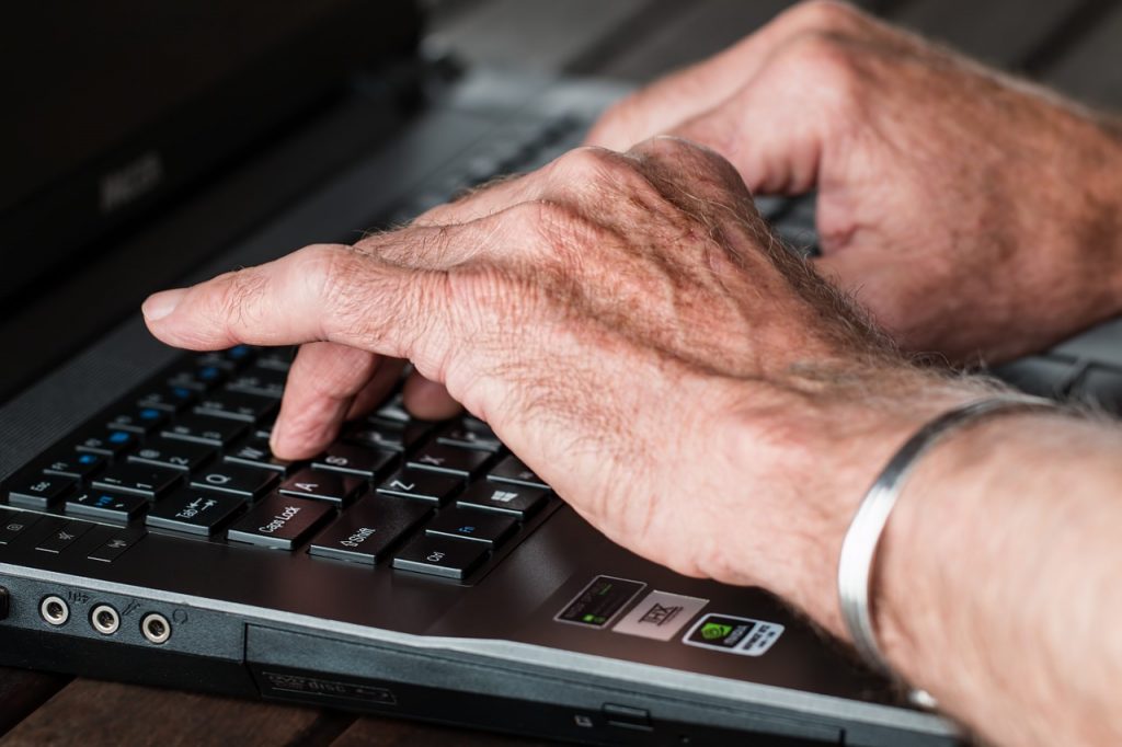 older man hands typing on a laptop computer