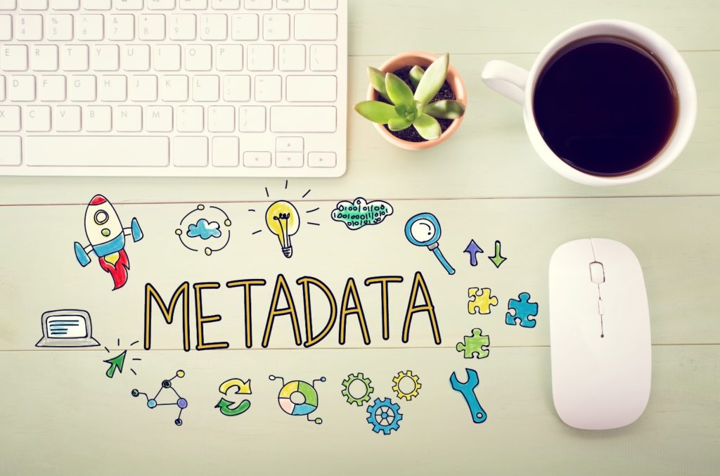 'metadata' written on a desktop with illustrations surrounding it. on the desk are also a cup of coffee, mouse, and keyboard.
